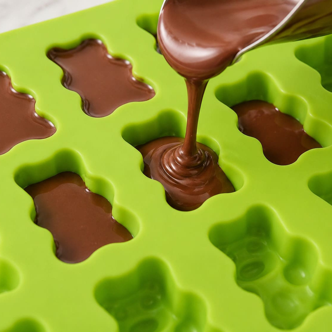 Flüssige Schokolade wird in eine Gummibärchen Silikonform gefüllt
