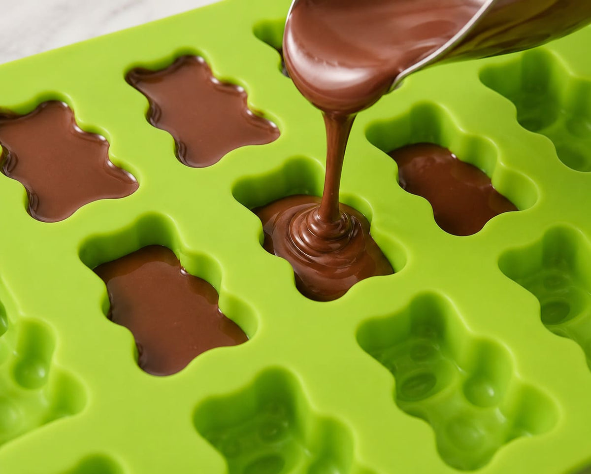 Flüssige Schokolade wird in eine Gummibärchen Silikonform gefüllt